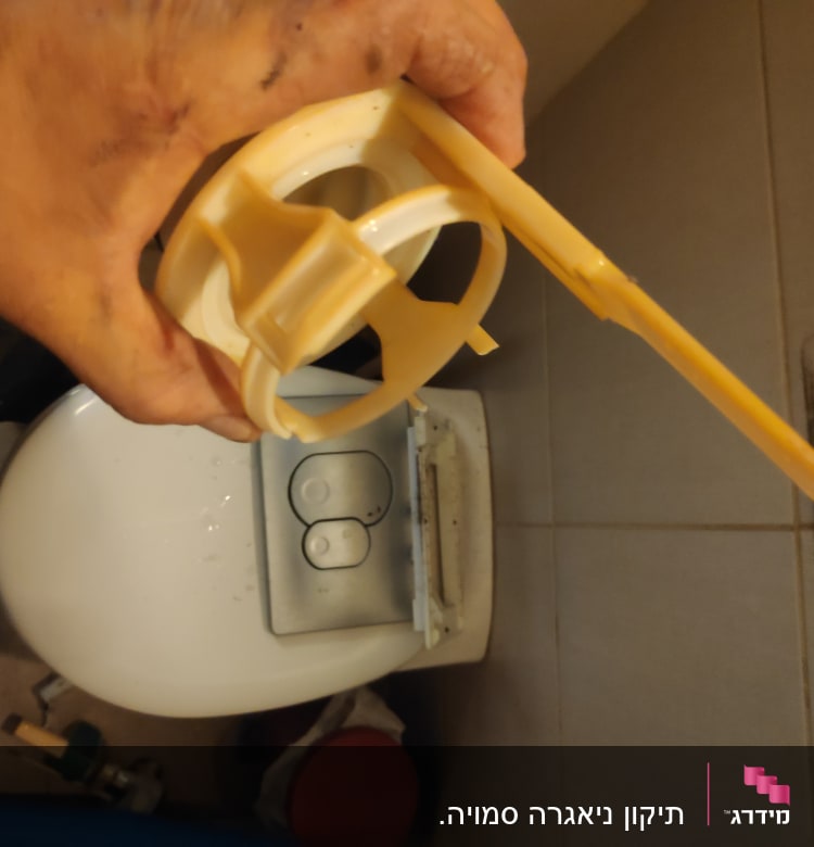 יד מחזיקה חלק פלסטיק ליד אסלה עם כפתור הדחה